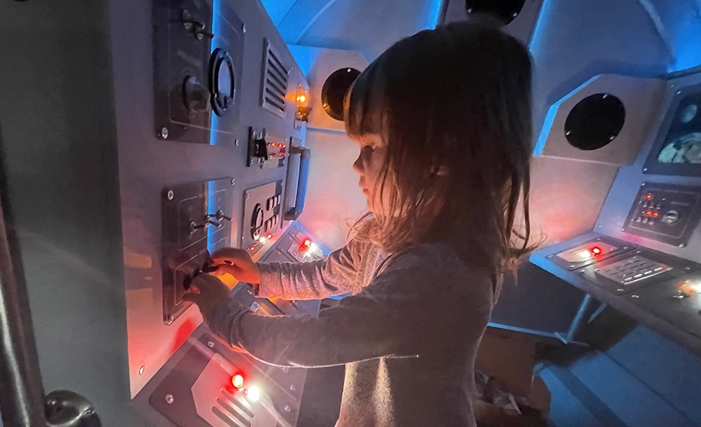 Niño jugando con la exposición Mission Control en la exposición Odisea del Espacio para Exploradores Galácticos en el CMOSC.